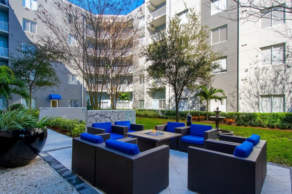 Courtyard seating area with chairs and fire pit. Grassy area with fountain in the background
