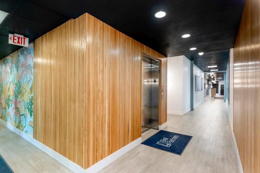 Interior elevator with wood walls and floral mural with door mat that says bell partners