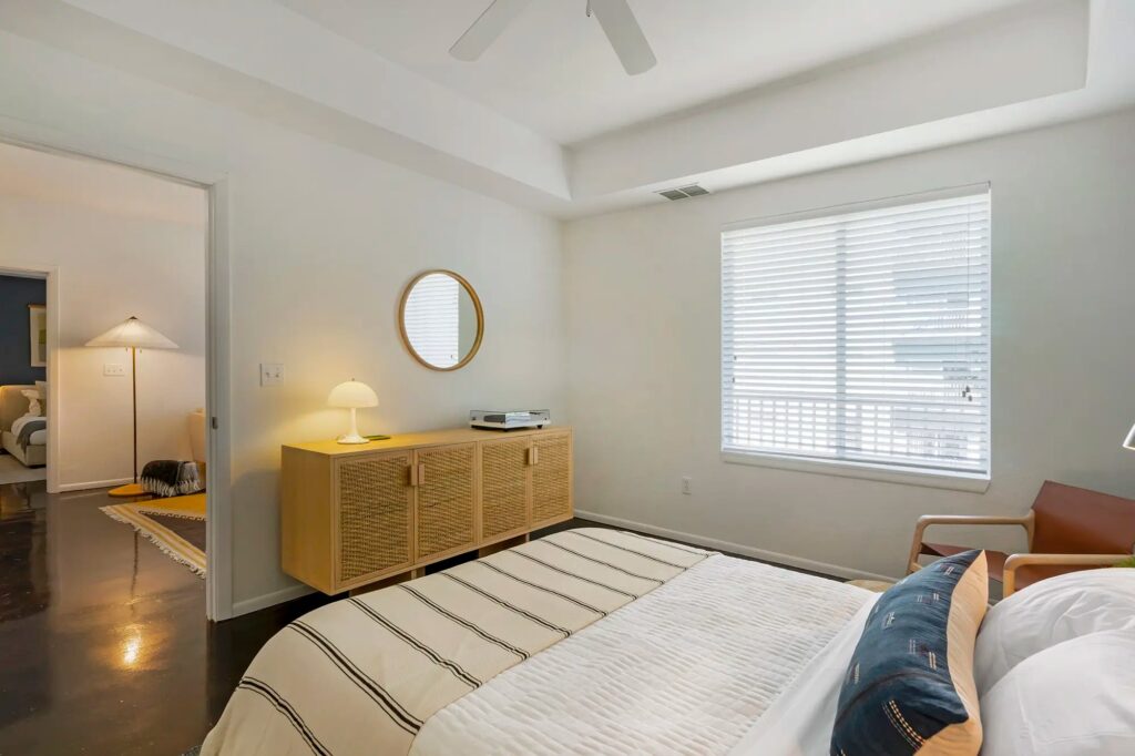 bedroom with large window, cement floors, and ceiling fan access to the living room