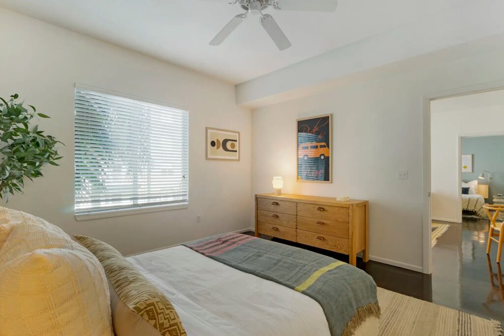 Bedroom with cement floors, large window, and ceiling fan with access to the dining room