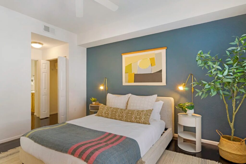 Bedroom with cement floors, large window, accent wall, and ceiling fan with access to closet and bathroom